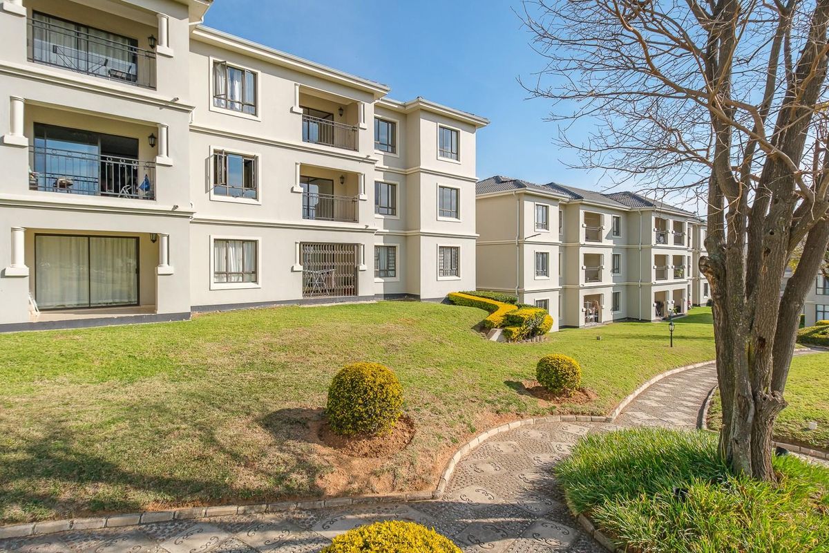 Exterior view of a multi-story apartment complex featuring private balconies, paved garden pathways, and well-maintained landscaped grounds.