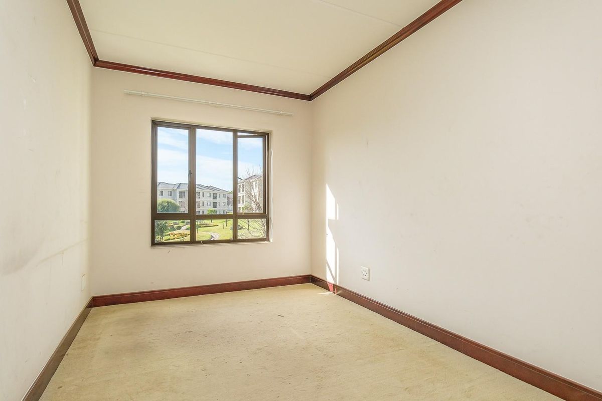 An empty bedroom featuring neutral walls, dark wood-look skirting boards, and a window with views of the complex grounds.