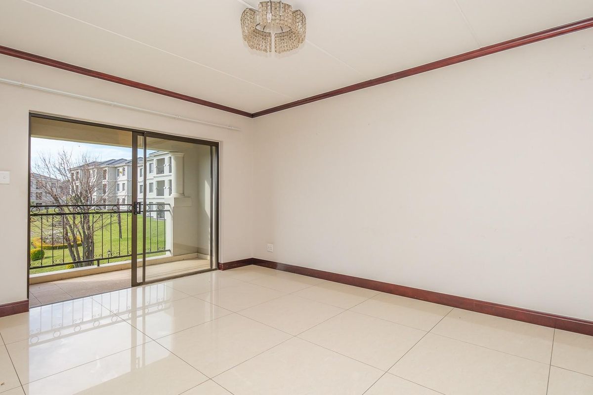A bright, empty living room featuring large format floor tiles, dark wood-tone skirting, and a sliding glass door leading to a private balcony.