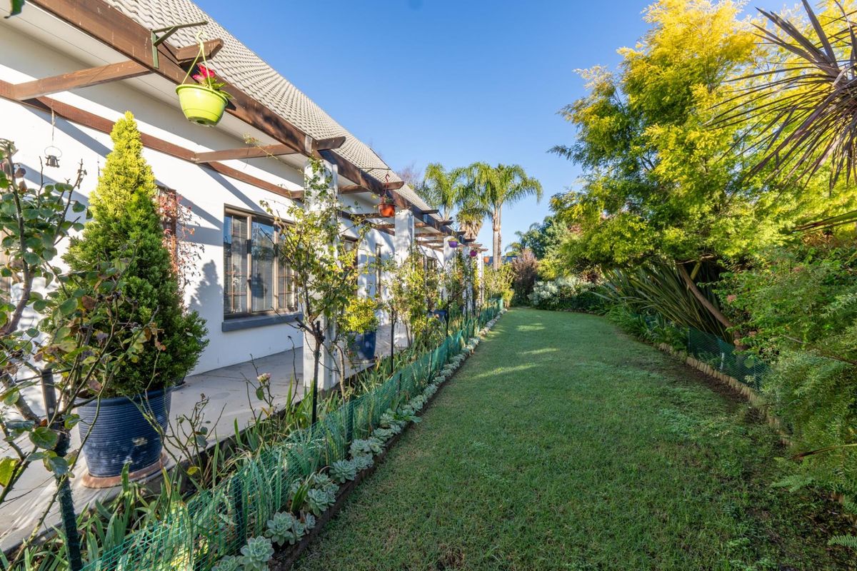 A well-maintained rear garden featuring a paved patio area with a timber pergola, overlooking a lush lawn and established perimeter landscaping.
