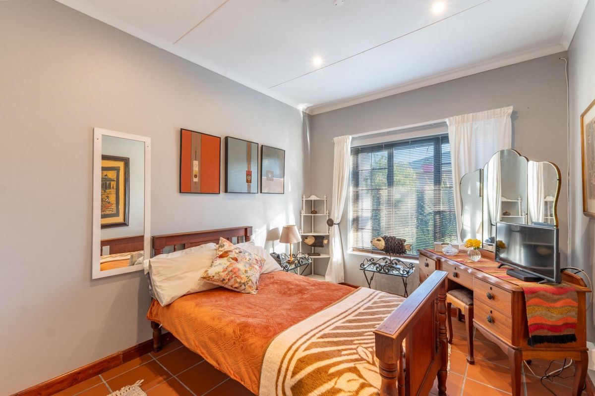 A cozy bedroom featuring terracotta floor tiles, recessed ceiling lighting, and a window with fitted blinds.