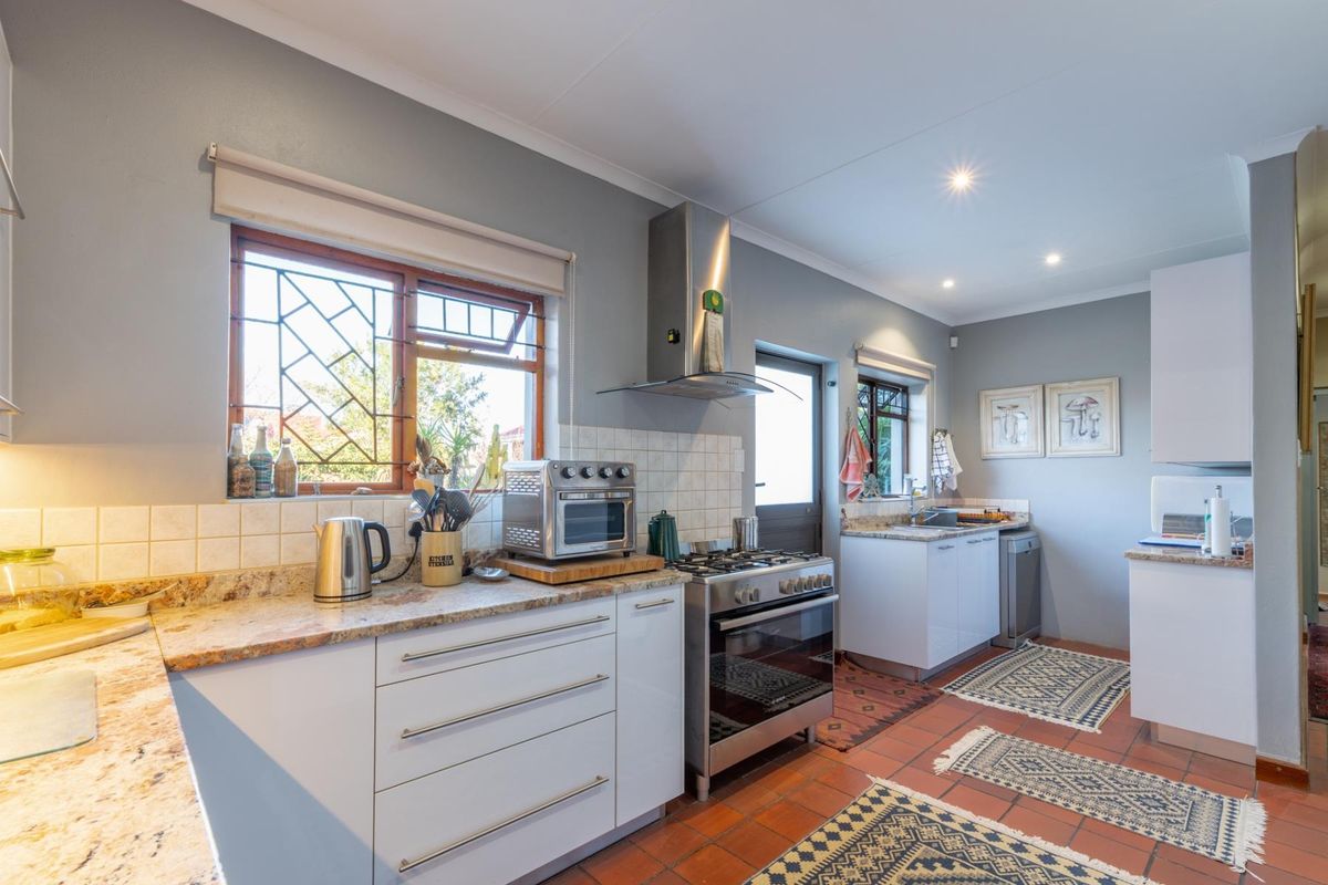 A functional kitchen featuring granite countertops, stainless steel gas stove with extractor fan, and tiled flooring with direct outdoor access.