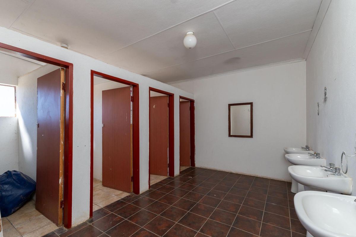 Communal bathroom facility featuring multiple stall entrances and a row of wall-mounted ceramic washbasins with tiled flooring.