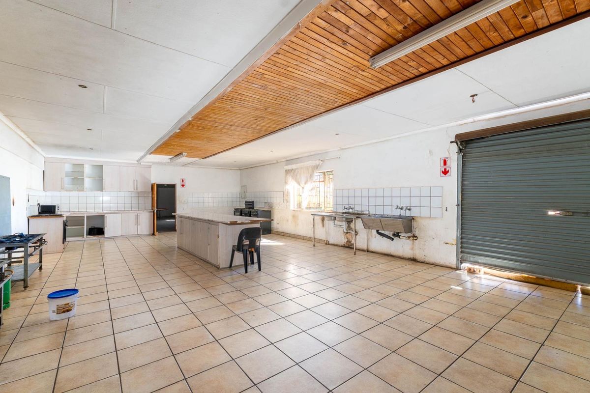 Spacious kitchen area featuring tiled flooring, built-in cabinetry, stainless steel sink, and a roller shutter door, offering significant potential for renovation.