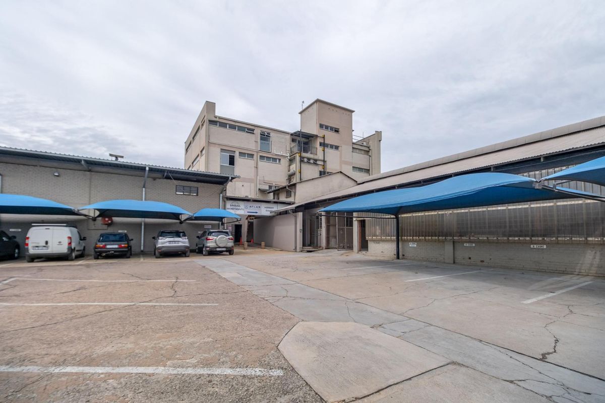 Exterior view of a commercial property featuring a paved parking area with blue shade cloth carports and multi-story industrial building structures.