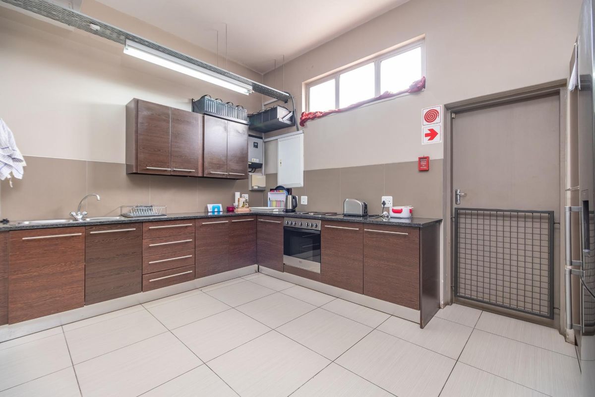 A functional kitchen area featuring dark wood cabinetry, granite countertops, a built-in oven, and tiled flooring, suitable for a retail or office environment.