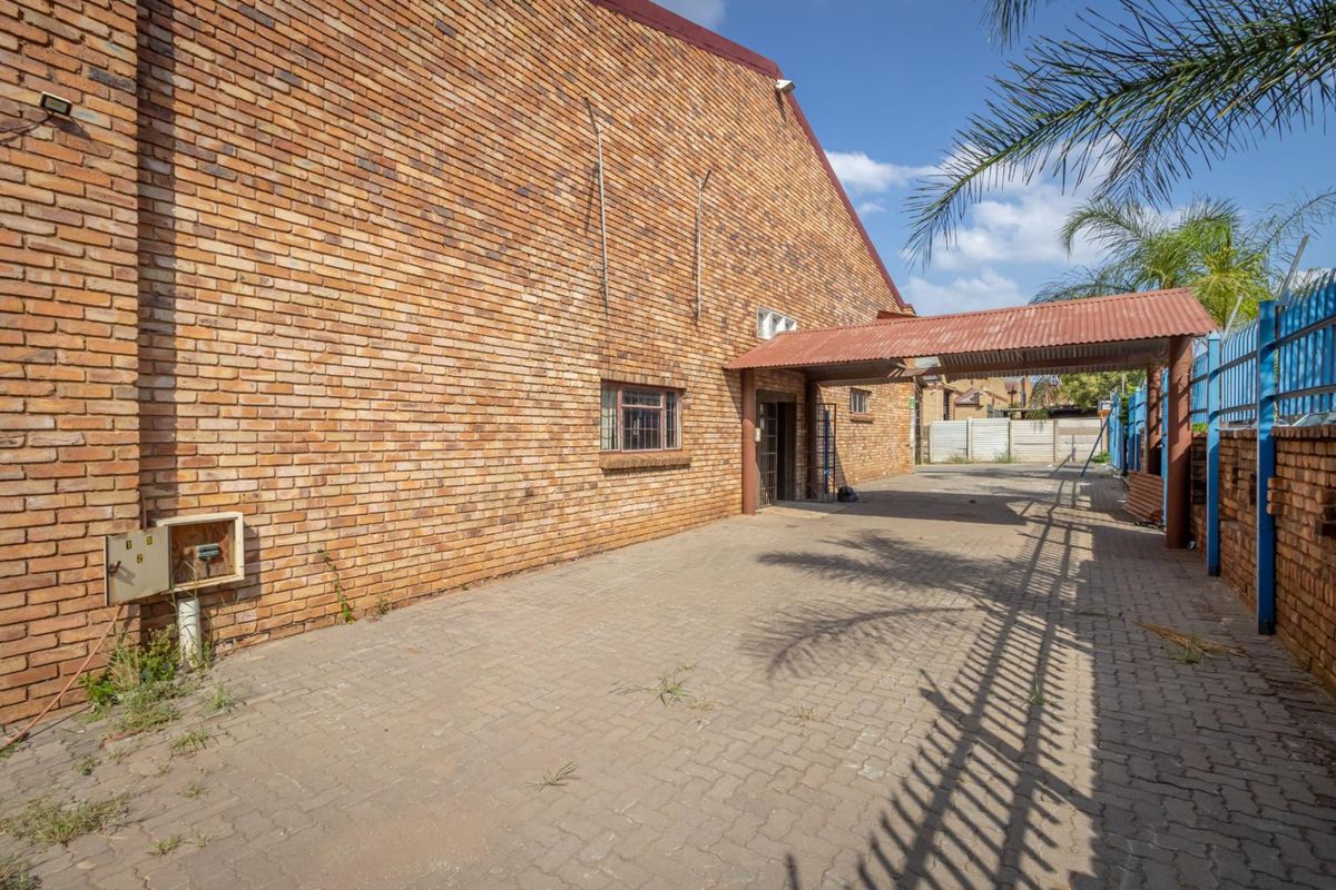 Side exterior view of the commercial property featuring a brick facade, paved driveway, and a covered walkway structure.