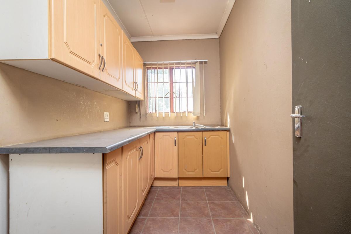 A compact kitchen area featuring light wood cabinetry, laminate countertops, a single basin sink, and tiled flooring with security bars on the window.