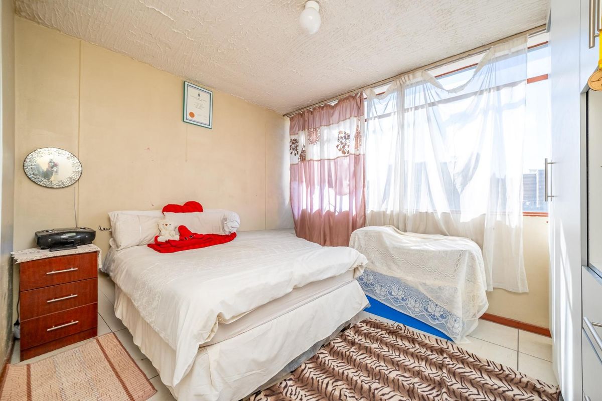 A bedroom featuring tiled flooring, large windows with natural light, and built-in cupboard space.