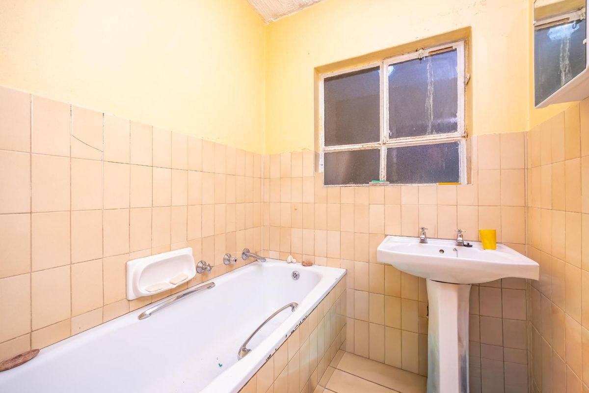 A dated bathroom featuring a standard bathtub with integrated handles, a pedestal basin, and tiled walls in need of modernization.