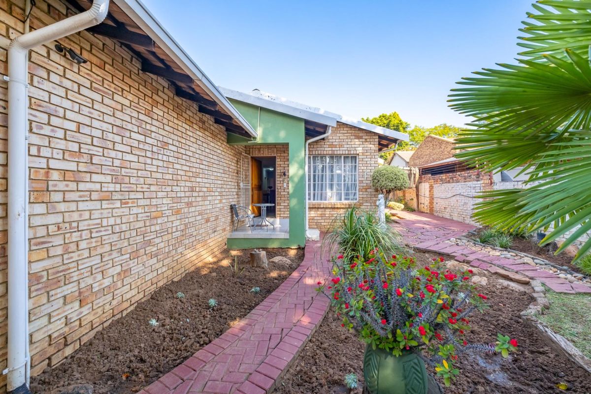 A view of the rear exterior featuring a brick facade, a paved walkway, and a landscaped garden area leading to the home entrance.
