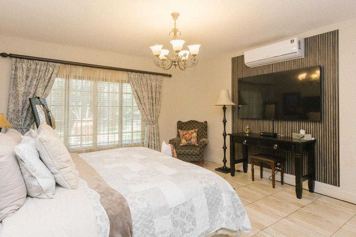 A well-maintained bedroom featuring tiled flooring, a decorative feature wall with a wall-mounted air conditioning unit, and large windows with curtain treatments.