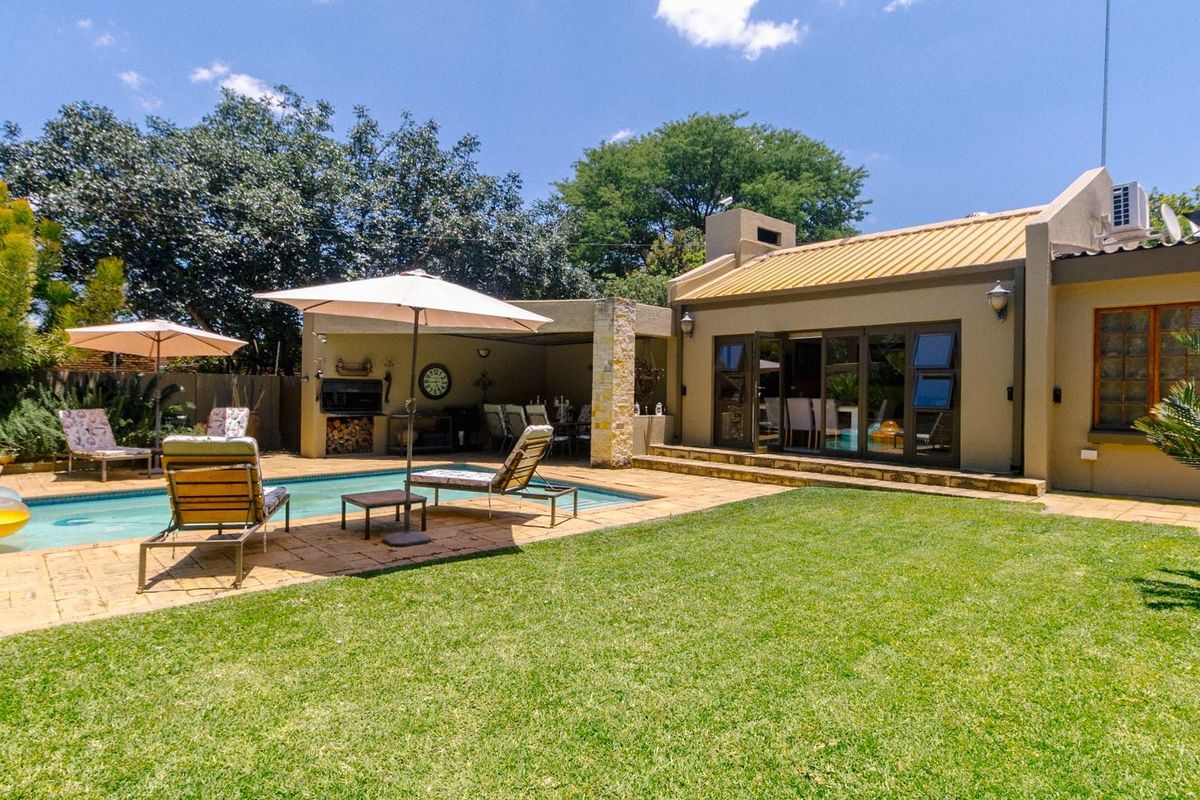 A well-maintained rear garden featuring a swimming pool, paved patio area, and a covered outdoor entertainment space with a built-in braai.