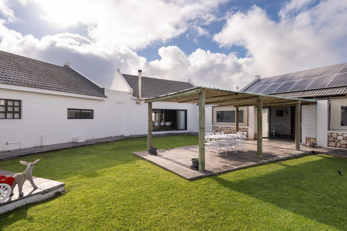 A spacious rear courtyard featuring a paved patio area with a timber pergola, well-maintained lawn, and solar panels installed on the roof.