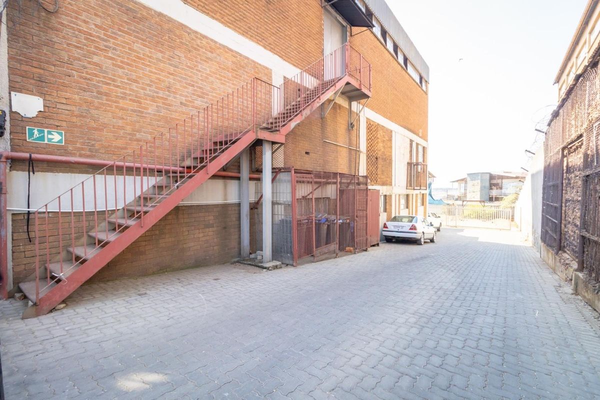 Rear exterior view of the retail property featuring a paved service area, metal external staircase, and secure storage enclosure.