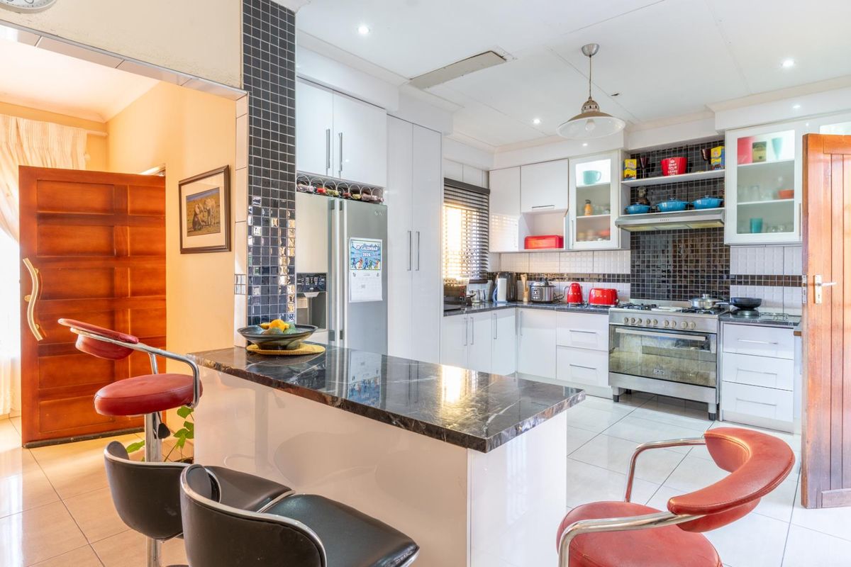A well-lit kitchen featuring white cabinetry, a dark stone breakfast bar, tiled backsplash, and a built-in gas stove with an extractor fan.