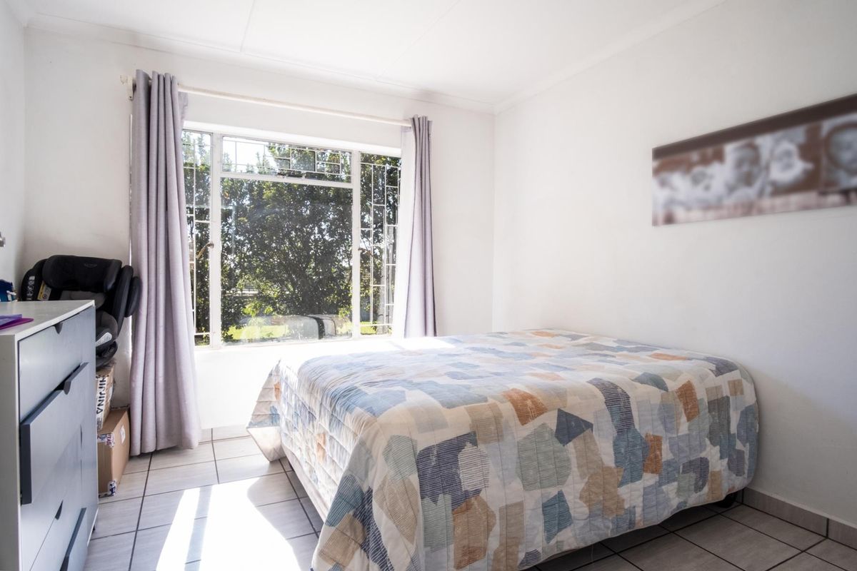A bright bedroom featuring tiled flooring and a large window with security bars, providing natural light and garden views.