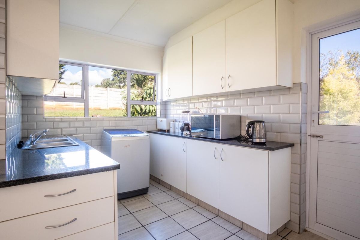 A functional kitchen featuring white cabinetry, dark countertops, subway tile backsplash, and a dedicated space for laundry appliances with direct outdoor access.