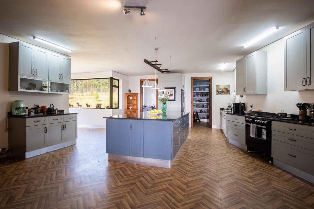 Spacious open-plan kitchen featuring a large central island, modern cabinetry, dark stone countertops, and herringbone-patterned flooring with an adjacent walk-in pantry.