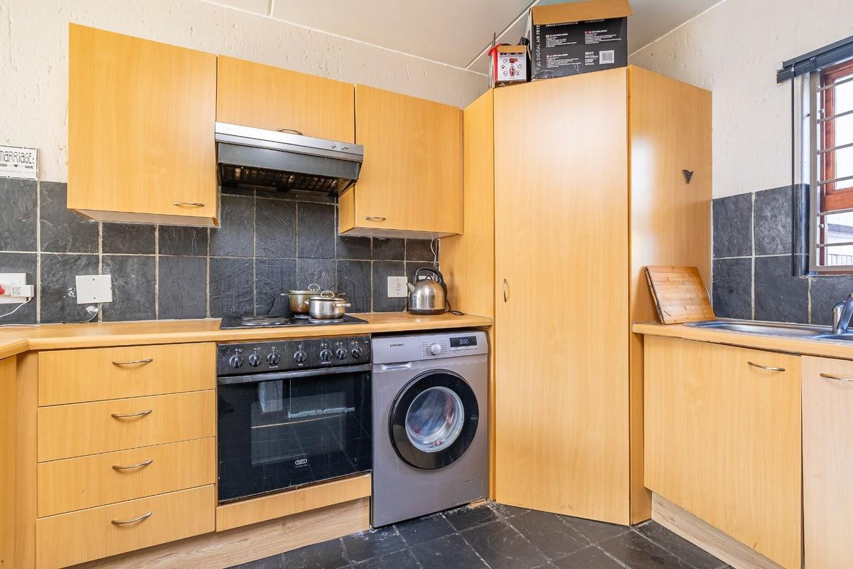 Functional kitchen featuring light wood cabinetry, dark tiled backsplash, built-in oven with hob, extractor fan, and integrated laundry appliance space.