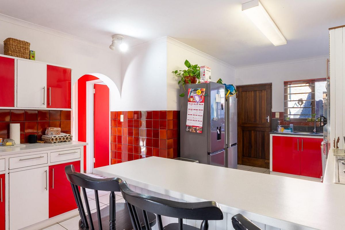 A functional kitchen featuring red and white cabinetry, a breakfast bar, and tiled splashbacks, offering a practical layout for daily meal preparation.