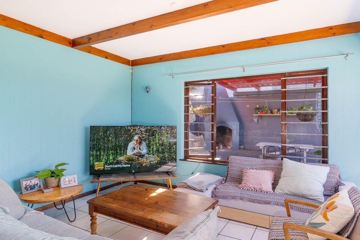 A living room featuring tiled flooring, exposed timber ceiling beams, and a large window looking out onto a rear patio area.