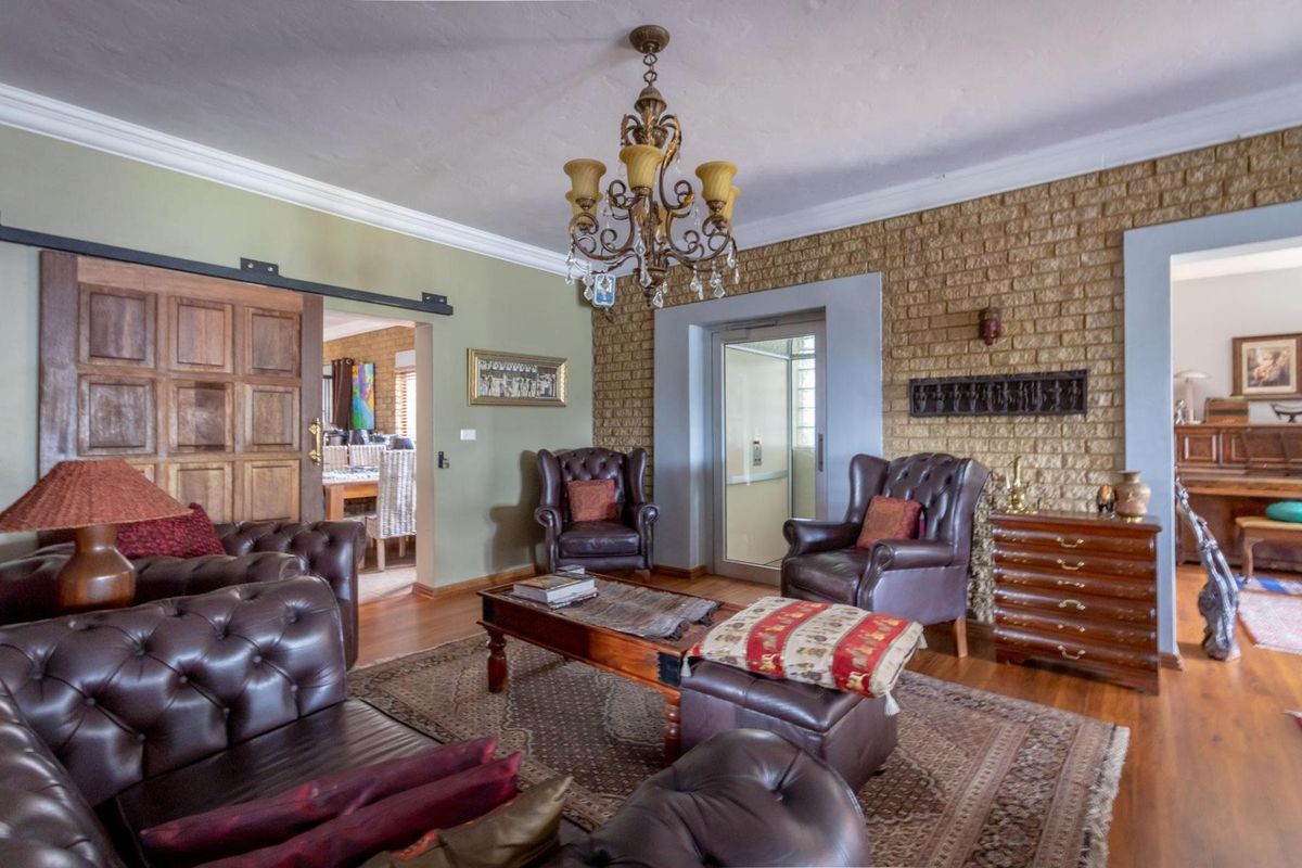 A spacious living room featuring a textured brick feature wall, wooden flooring, crown molding, and a classic chandelier.