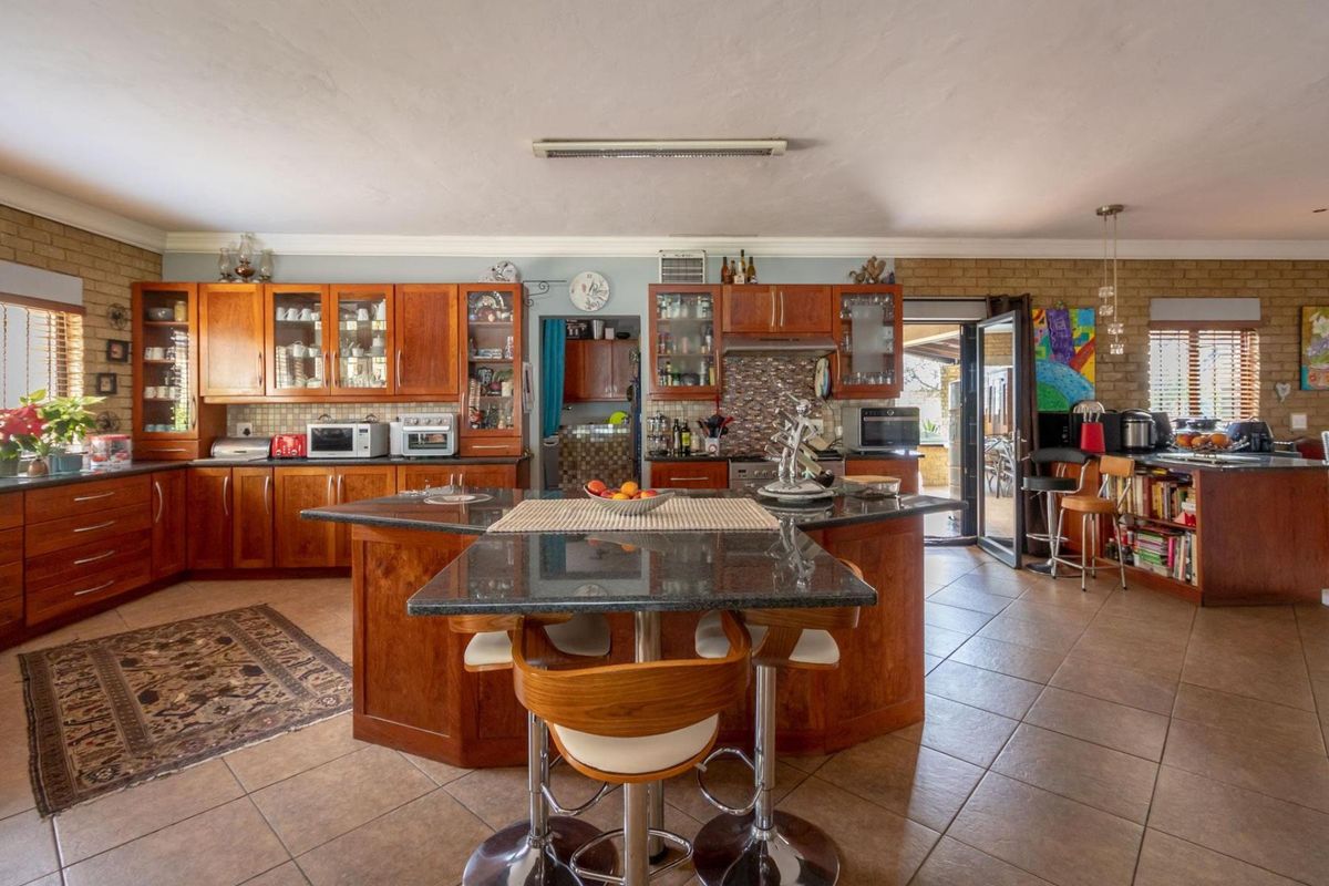 Spacious kitchen featuring timber cabinetry, granite countertops, a central island with breakfast bar seating, and direct access to the outdoor patio area.