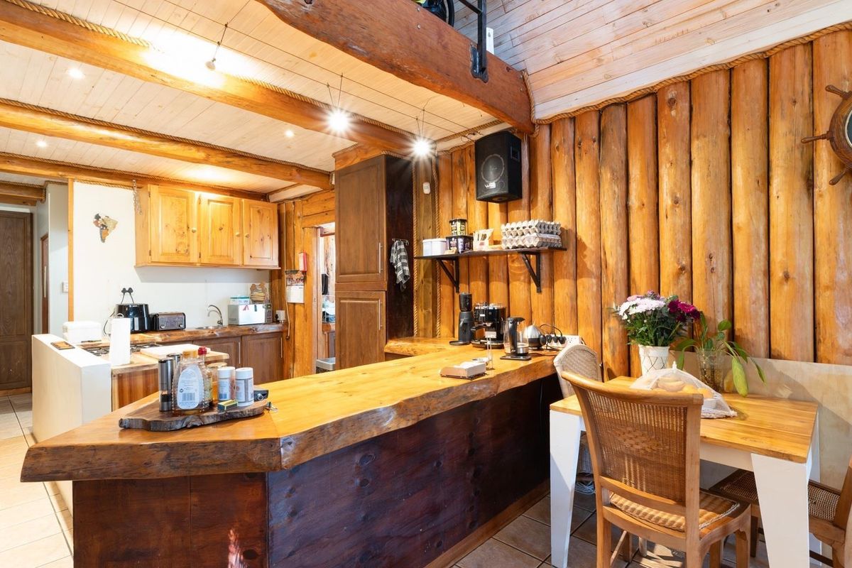 Rustic kitchen featuring distinctive log walls, exposed timber ceiling beams, and a custom live-edge timber breakfast bar with integrated cabinetry.