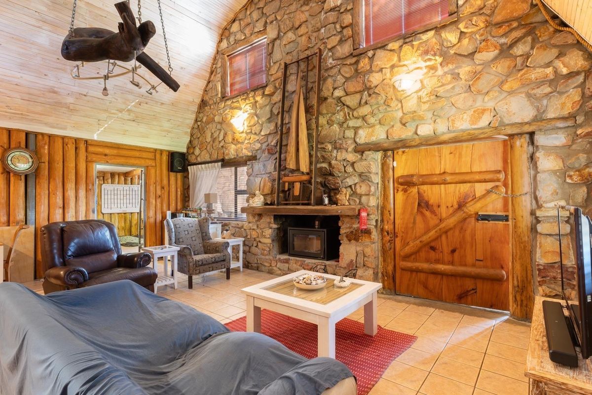 Rustic living room featuring a prominent stone fireplace with a wood-burning stove, timber wall cladding, and exposed wooden ceiling beams.