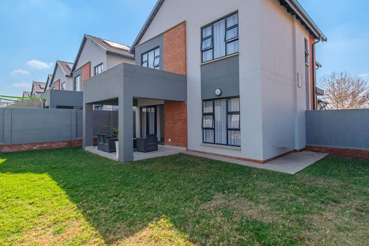 Rear view of a modern double-storey townhouse featuring a covered patio, private garden, and secure boundary walls.