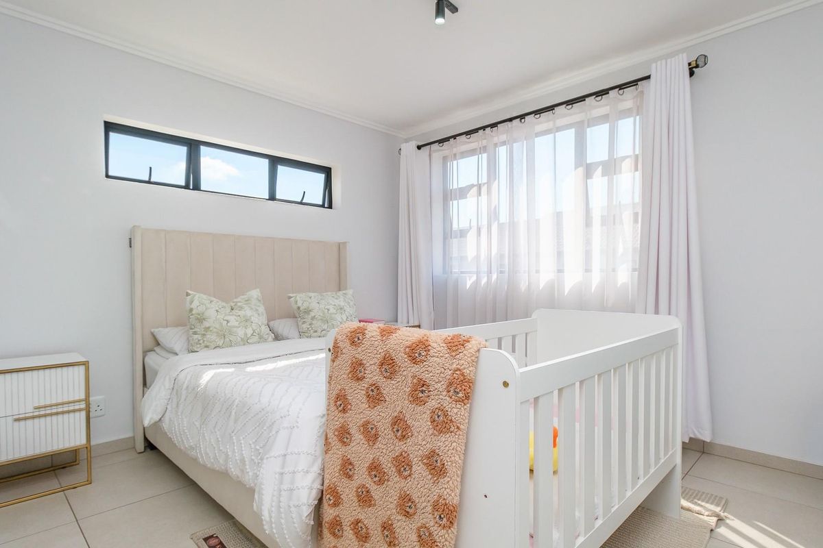 A bright and well-maintained bedroom featuring tiled flooring, a horizontal clerestory window, and a large window with fitted curtain rods.