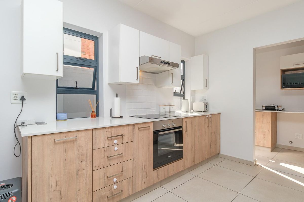 Modern kitchen featuring light wood-finish cabinetry, stone countertops, subway tile backsplash, and integrated appliances, with an adjacent scullery area.