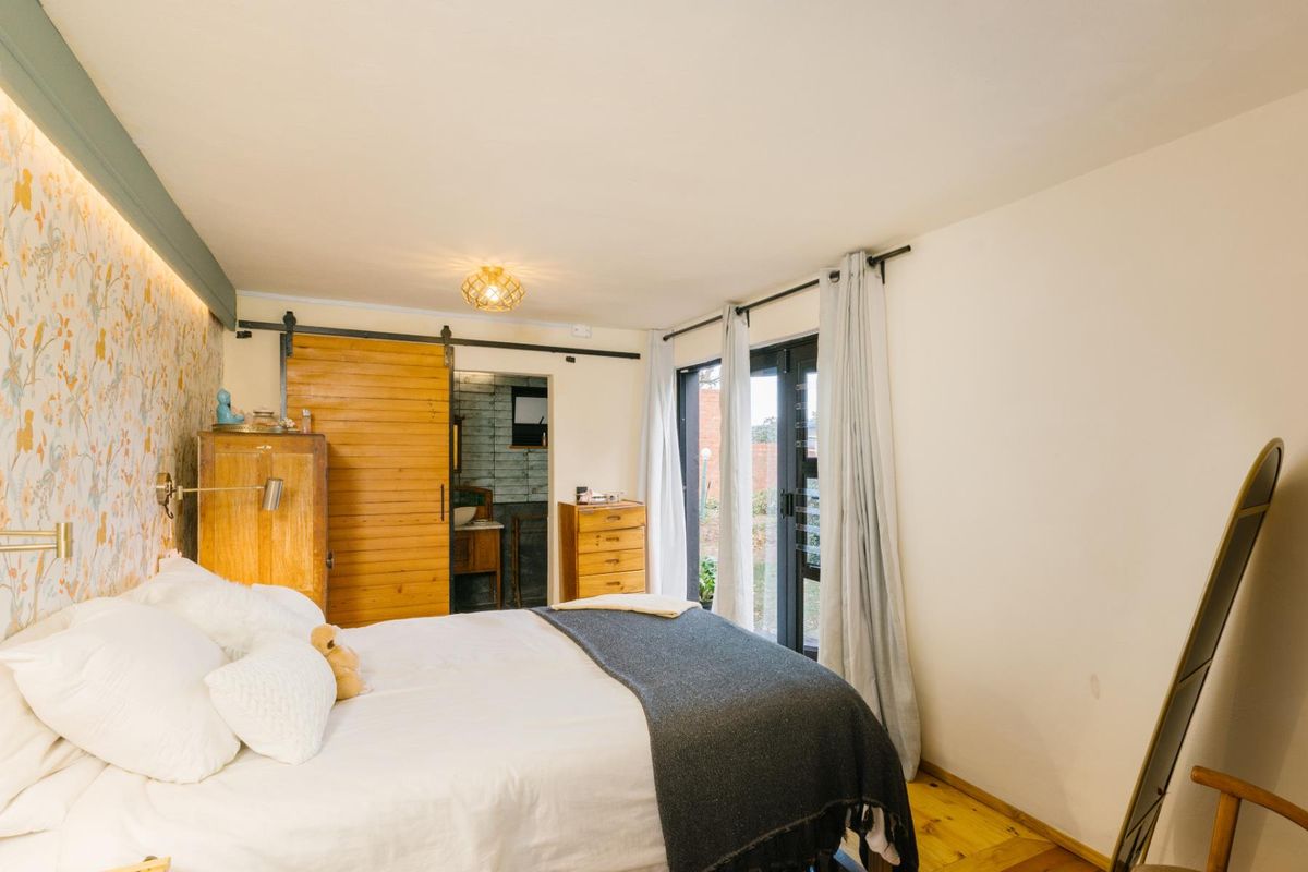 A well-lit bedroom featuring hardwood floors, an accent wall with patterned wallpaper, a sliding barn door, and direct access to the outdoors via french doors.