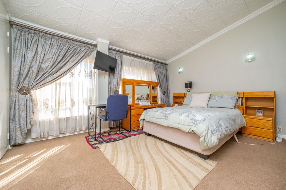 A spacious bedroom featuring neutral carpeting, built-in wooden headboard shelving, and decorative ceiling tiles.