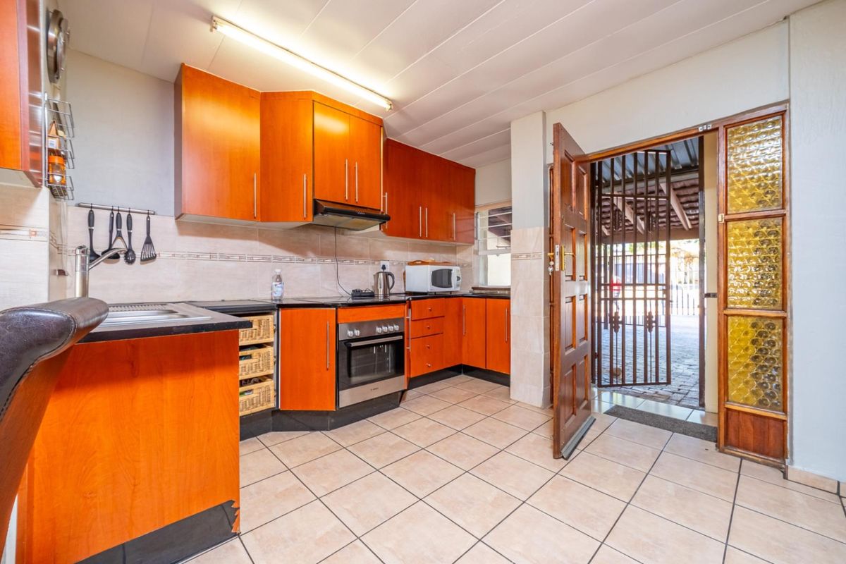 Functional kitchen featuring wood-veneer cabinetry, built-in oven, extractor fan, and tiled flooring with direct access to an exterior area.
