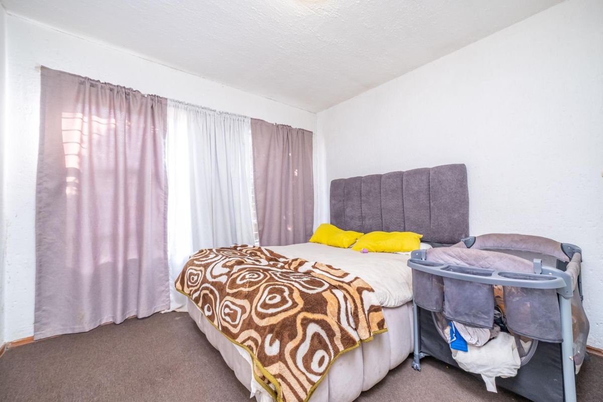 A standard bedroom featuring carpeted flooring and large windows with installed curtain tracks, providing a functional space for rest.