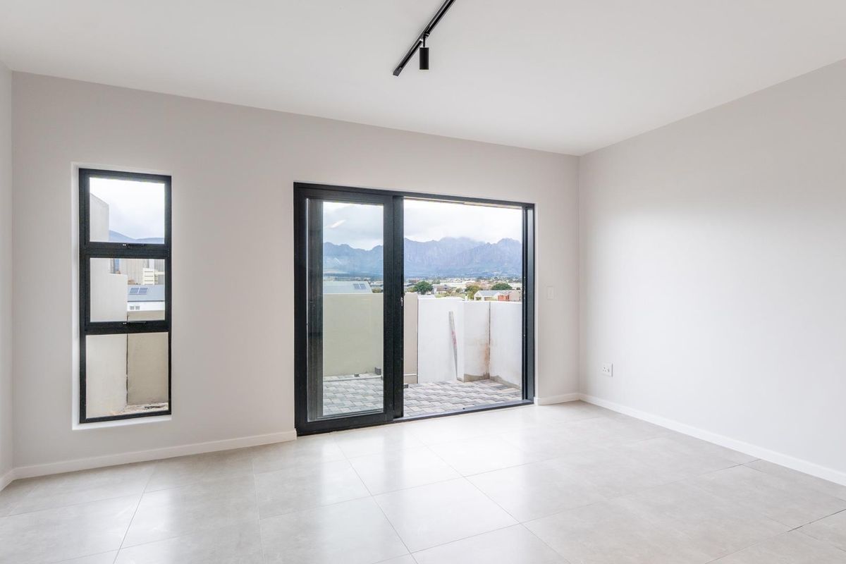 A bright, modern bedroom featuring neutral tiled flooring, minimalist track lighting, and large sliding glass doors that open onto a private balcony with mountain views.