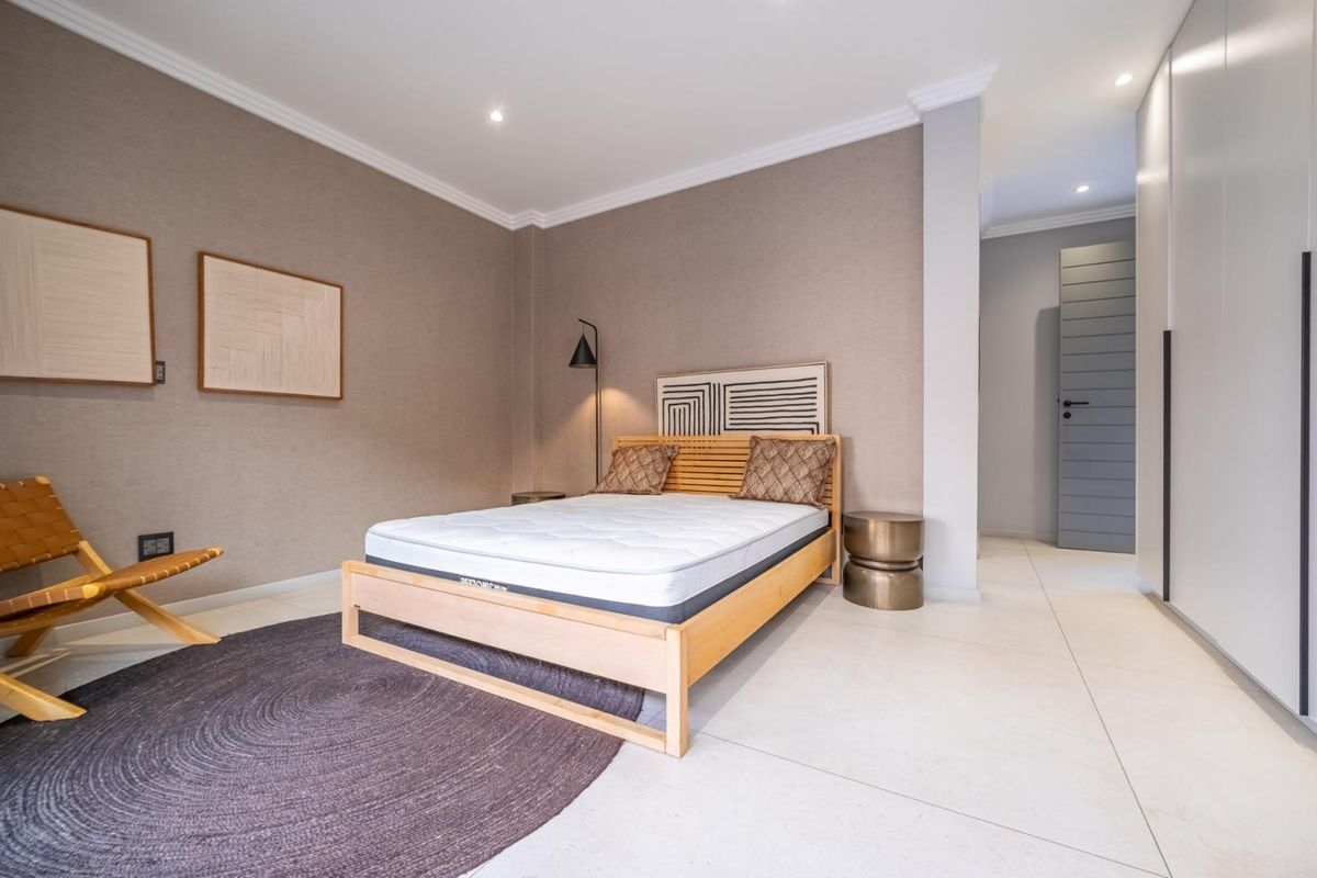A modern, well-maintained bedroom featuring neutral textured wallpaper, large format floor tiles, recessed ceiling lighting, and built-in floor-to-ceiling wardrobes.