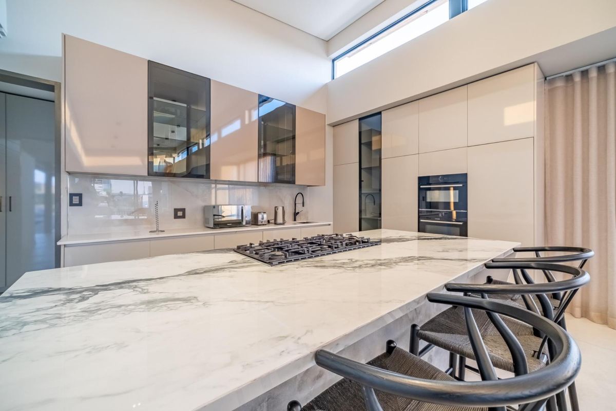 Modern kitchen featuring a large marble-topped island with an integrated gas hob, sleek cabinetry, and high-end built-in oven.