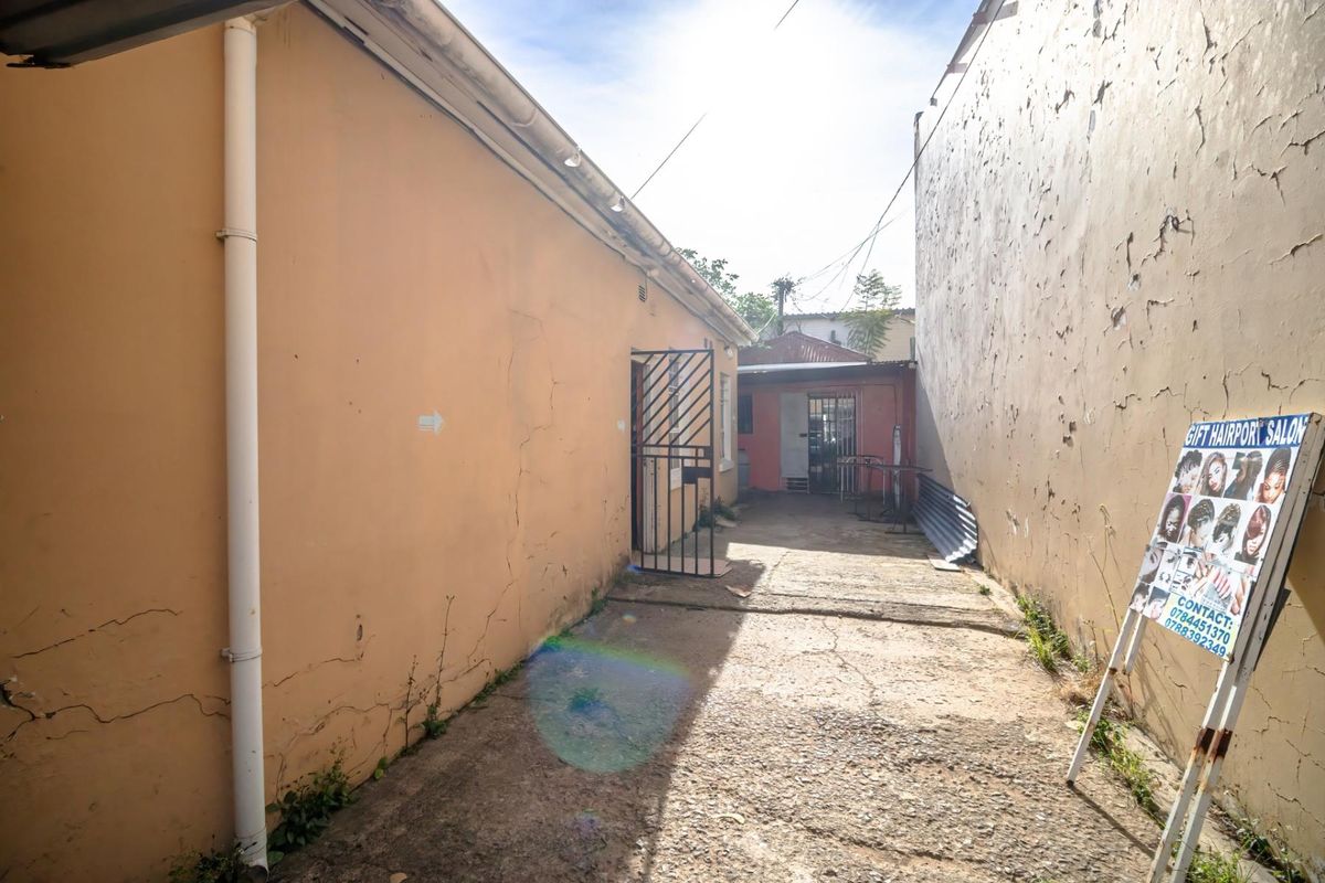 Exterior side alleyway featuring concrete paving, security gates, and weathered boundary walls, providing access to the rear of the commercial property.