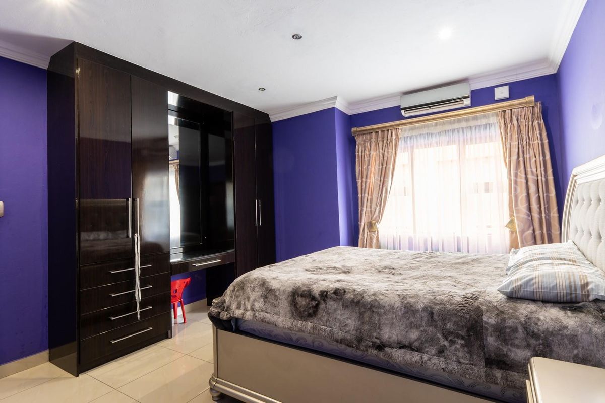A bedroom featuring dark wood built-in cabinetry with an integrated vanity, tiled flooring, and a wall-mounted air conditioning unit.