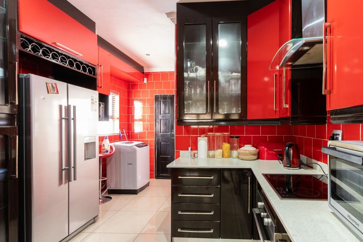 A vibrant kitchen featuring high-gloss red cabinetry, black accents, tiled walls, stone countertops, and an integrated laundry area with tiled flooring.