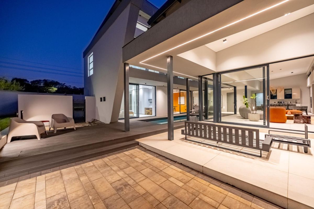 Modern architectural rear exterior featuring a covered patio, timber decking, paved courtyard, and seamless indoor-outdoor flow through large sliding glass doors.