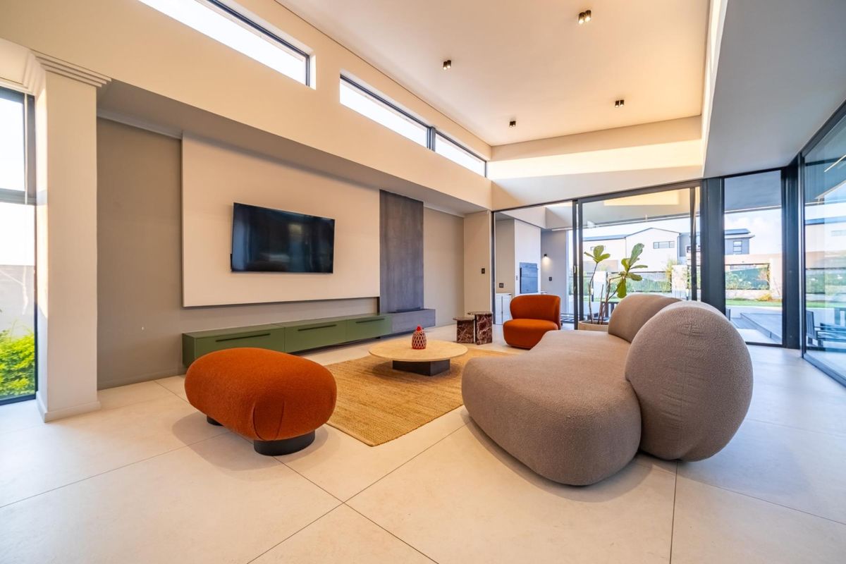 Modern living room featuring high ceilings, clerestory windows, large format floor tiles, and seamless indoor-outdoor flow through sliding glass doors.
