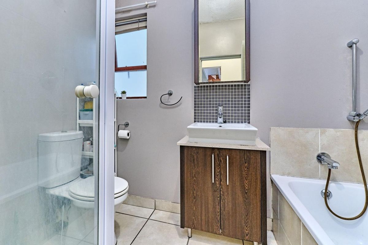 A functional bathroom featuring a vanity with a vessel sink, a tiled bathtub with a shower attachment, and a separate glass-enclosed toilet area.