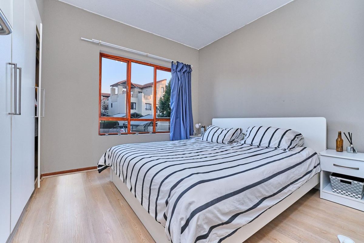 A bedroom featuring light wood-look flooring, built-in cupboards, and a large window with views of the surrounding townhouse complex.