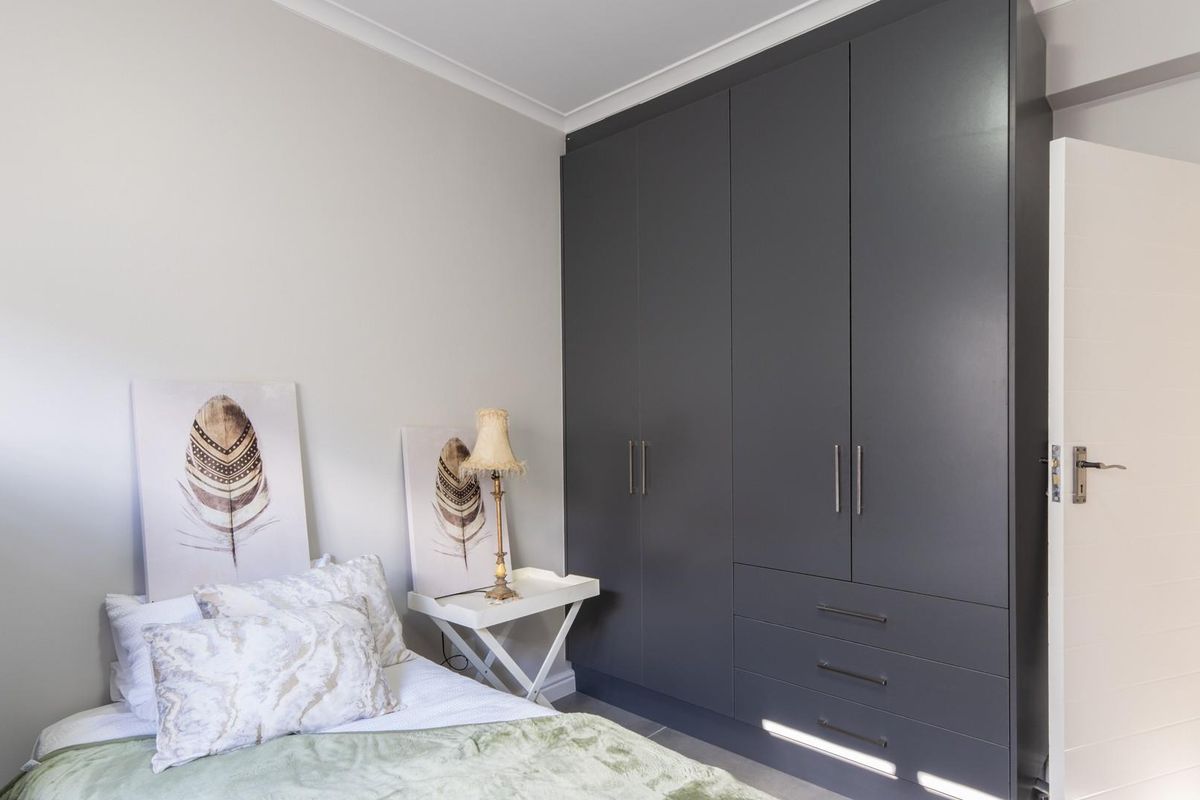 A well-maintained bedroom featuring modern floor-to-ceiling dark grey built-in cabinetry with integrated drawers and a view into the adjacent bathroom.