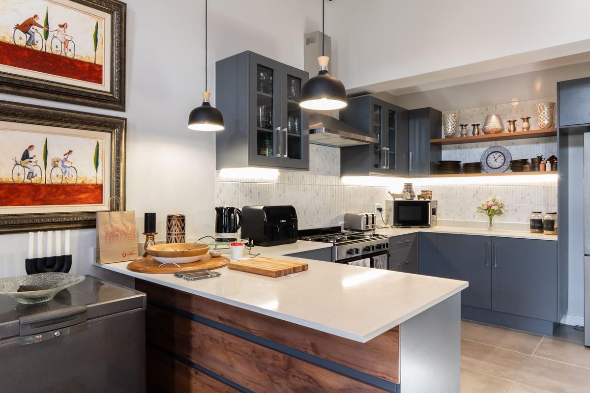 Modern kitchen featuring dark grey cabinetry, stone countertops, a breakfast bar, integrated lighting, and a stainless steel gas stove with extractor fan.