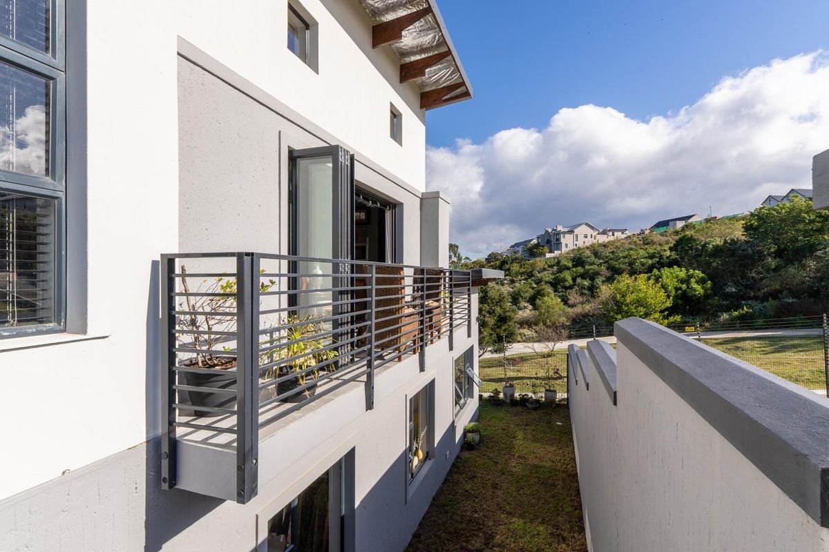 A side view of the property featuring a modern balcony with metal railings, large glass sliding doors, and a view of the surrounding landscape.